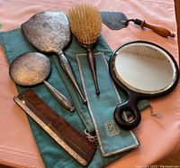 Full view of sterling silver vanity set pieces on blue storage bags with ebony framed hand mirror and wooden handled cake server