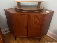 Full view of wood corner cabinet with closed doors, showing shape and wood grain.