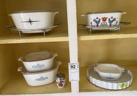 CorningWare baking dishes showing various patterns including blue cornflower and a floral design with metal racks and an egg coddler