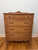 Front view of the light wood dresser showing all four drawers and decorative details on the top edge and front panels.