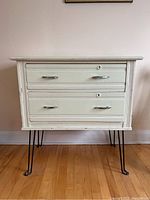 Front view of the painted wood dresser with two drawers and metal handles, showing mid-century modern hairpin legs.
