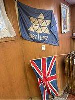 Canadian Confederation flag and Union Jack flag hanging on a wooden wall with part of a window and picture visible.