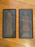 Two framed rubbings side by side on wooden floor showing full artwork and frames