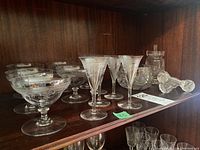 Shelf with multiple French crystal stemware glasses including etched aperitif and drinks glasses, plus some small glasses at back