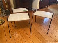 Three light beige vinyl cushioned stools with slender black metal legs on wood floor in room, showing overall look and condition.