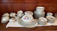 Full view of Meito china set including plates, cups, platters, tureens and other accessories displayed on a table with wooden background.