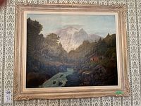 Full view of the framed oil painting showing the mountain river landscape under glass with a decorative wood frame.