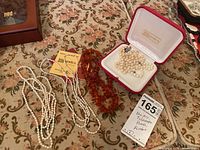 Lot of four necklaces displayed on floral fabric: three freshwater pearl necklaces including one in a red Majorica box, and one necklace made of amber beads.