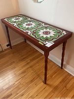 Angle view showing the three-part ceramic tiled tabletop with floral motif and turned wooden legs.