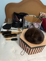 Vintage purses, shoe brushes, shoe trees, brown mink hat on striped hat box on mattress
