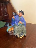 Front view of the Royal Doulton figurine showing the elderly woman in blue shawl, basket of goods, and pigeons.