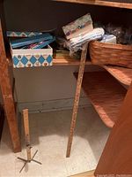 Wooden hemming guide leaning against shelving and a smaller wooden hemming guide with metal base on floor