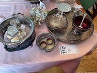 Overview of silver plate items on table including trays, bowl with ladle, napkin rings, cast dishes and a glass bowl on stand