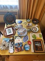Full view of all souvenir items on tabletop showing diverse plates, framed artworks, and ceramic decor pieces