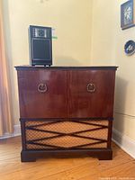 Wooden stereo cabinet by GE with a decorative front panel and a single black speaker placed on top.