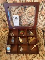 Overview of open brown wooden jewelry box with watches and jewelry inside, showing nine compartments and clear glass lid.