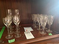Photo showing two sets of stemware on a wooden shelf: on the right, five Waterford crystal aperitif glasses about 5 inches tall with cut crystal patterns; on the left, plain and patterned Swedish stemware glasses between 5 and 7 inches tall.