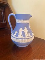 Full profile view of blue Wedgwood Jasperware pitcher decorated with white classical figure reliefs and ornamental borders.