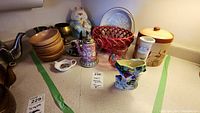 Full view of all items arranged on countertop with visible price tags. Includes wooden bowls, cat cookie jar, various ceramic and metal serving pieces, and vases.