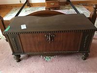 Front view of antique cedar chest showing decorative carvings, scalloped top edge, and rounded feet.