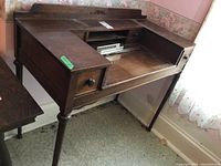 Front angled view of antique desk showing drawers, worn surface, and carved details.