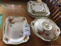 Photo showing stack of five dinner plates and five side plates along with covered casserole dish and serving tray, all with floral patterns and green and gold rim accents.