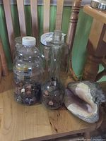 Photo of two jars filled with pennies and large conch shell on wooden chair