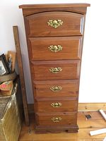 Front view of six drawer wooden dresser showing brass handles and wood grain finish.