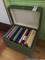 Open green vinyl-covered stool with vinyl record albums neatly arranged inside.