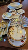 Various ceramic platters, bowls, glass bowl, plates, dessert plates, and assorted cutlery with decorative handles on a wooden table.