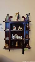 Front view of the wooden decorative wall shelf with figurines and thimbles inside