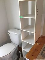 Photo showing side view of white shelving unit beside toilet and wooden ledge in bathroom.