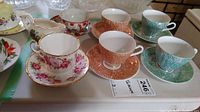 Overview of all teacups, saucers, and the creamer arranged on a table.