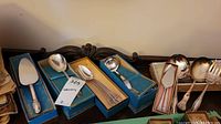 Boxed and loose Rogers Bros plated serving utensils including spoons and spreaders.