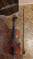 Top view of the vintage violin and bow on a tiled floor showing the condition of both items.