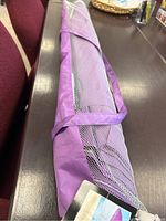 Purple beach umbrella folded in mesh and fabric protective cover, placed on a dark wooden surface.