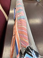 Rolled up beach umbrella with multicolor stripes in a white mesh carrying bag, showing the rolled fabric and partial strap.