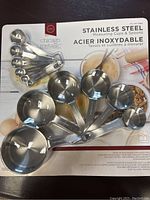 Top-down photo of 12 stainless steel measuring cups and spoons in original packaging, all nested and attached to a ring.