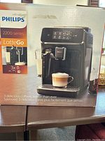 Front view of unopened box showing Philips 2200 Series LatteGo espresso machine in black with milk frother