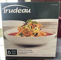 Front view of the Trudeau brand box showing the 6 piece set of porcelain dinner bowls and a bowl with salad inside.