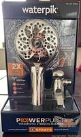 Front packaging shows chrome Power Pulse shower head with multiple spray nozzles and included hose, highlighting 2X massage force and 8 spray settings.