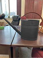 Side view of the black and bronze watering can on a table showing handle and spout.