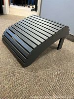Grey wooden slatted footstool shown from a front and side angle on carpeted floor.