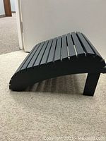 Side view of grey footstool showing slatted design and curved shape.