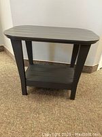 Front and side view of the grey patio side table showing the slatted lower shelf and curved edges on the top surface.