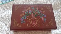 Top of hand painted wooden jewelry box showing floral and gold Celtic knot designs.