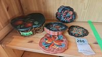 Set of five hand painted Gisela D. ceramic coasters with floral designs and an apple shaped wire basket with a matching painted ceramic lid.