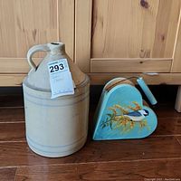 Pottery jug with handle and heart-shaped caddy set on wooden floor in front of wooden cabinets.