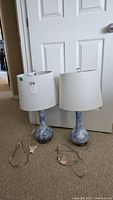 Two matching ceramic table lamps with blue and white marbled bases and white shades placed on carpeted floor.