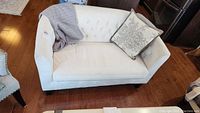 Front angle view of white loveseat with decorative pillow and blankets on top.